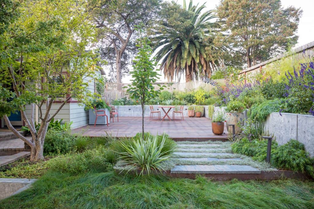 picture of a professionally landscaped garden with a medaw, stone path, deck, and concrete retaining walls